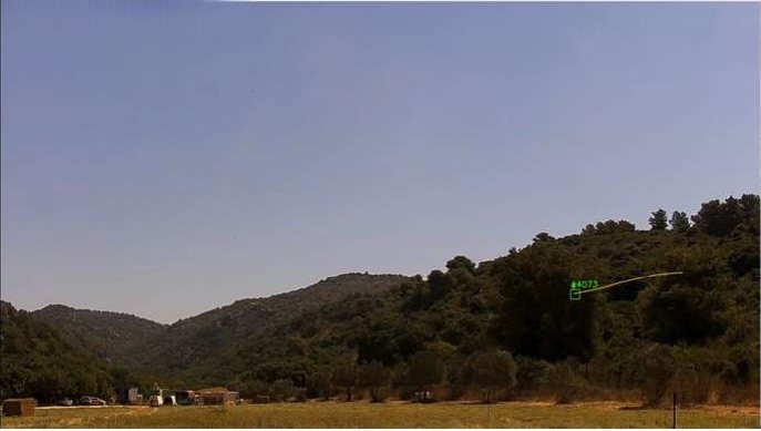 Drone detection field test: PTZ camera frame with a green Track Motion box and trail over a wooded hill